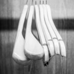 Felipe Peña contemporary art: Six wooden clothes hangers hang closely together on a metal rod against a wooden background. The image is in black and white, emphasizing the smooth, rounded shapes of the hangers and the grain of the wood. , exclusive contemporary art for New York collectors