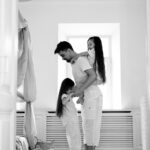 Felipe Peña contemporary art: A man stands in a bright room hugging a young girl, while another girl sits on his shoulders. All three wear light pajamas. Toys and a basket are on the floor nearby. The atmosphere feels cozy and affectionate. The image is in black and white. , exclusive contemporary art for New York collectors