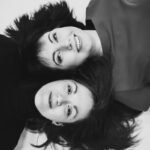 Felipe Peña contemporary art: Two women lie on their backs, head-to-head, with dark hair fanned out. Both are smiling and looking up at the camera. One wears a dark top, the other a lighter blouse. The image is black and white with a soft, bright background. , exclusive contemporary art for New York collectors